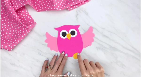 hand gluing feet onto pink paper owl 