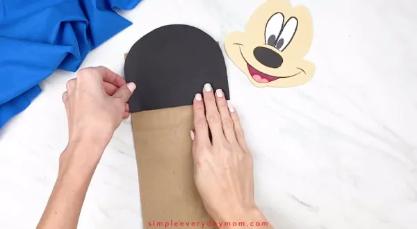 hands gluing paper mickey head onto paper bag craft