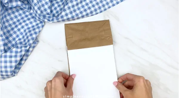 Hands gluing white paper onto paper bag 