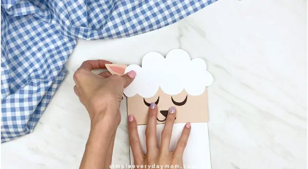Hands gluing ears to back of paper bag sheep craft 
