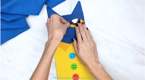 hands gluing paper Pete the Cat eyes onto puppet craft