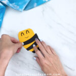 Hands gluing stripes onto paper bee