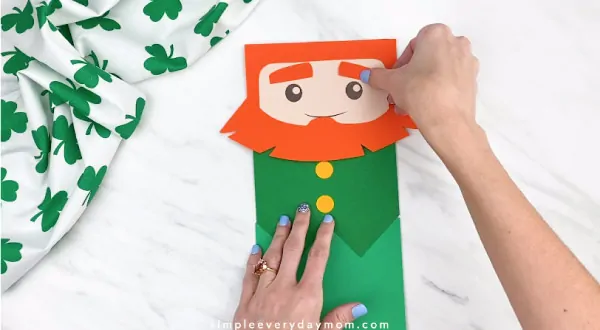 Hands gluing eyebrows onto paper bag leprechaun craft 