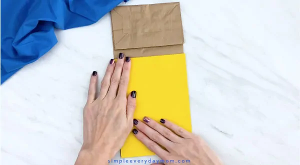 Hands gluing yellow paper to brown paper bag