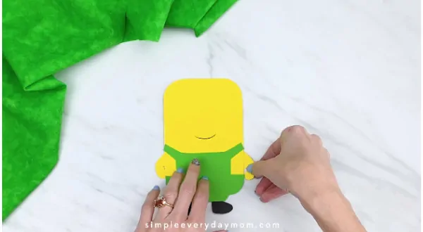 Hands gluing arms to paper minion craft 
