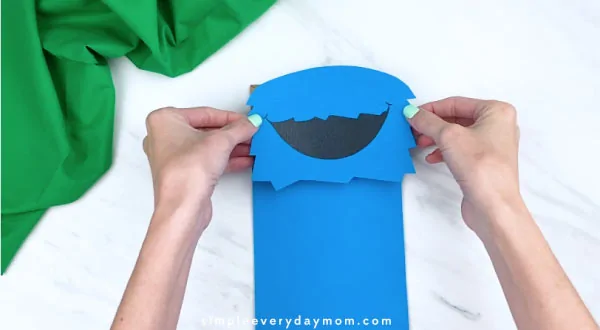 hands gluing on cookie monster head to paper bag 