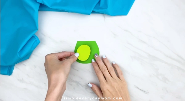 Hands gluing light green circle to dark green shape 