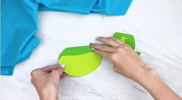 Hands gluing light green paper to dark green paper 