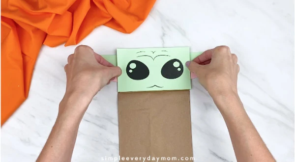 Hands gluing yoda face to brown paper bag 