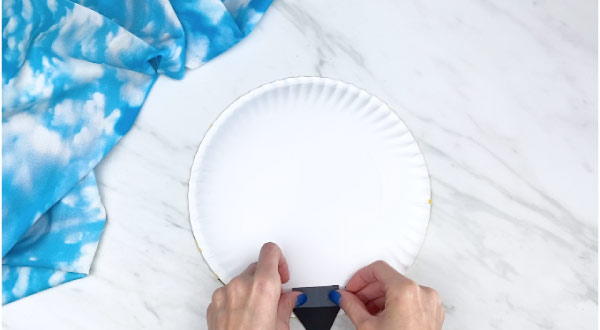 Hands taping bee stinger to back of paper plate 