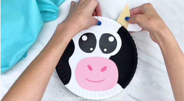 Hands gluing horn/ear to back of paper plate cow 