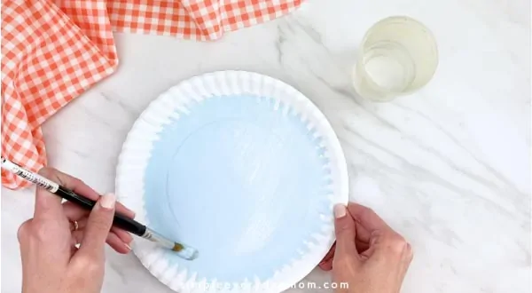 Hands painting paper plate light blue 