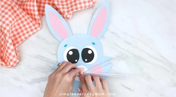 Hands gluing on pipe cleaner whiskers to paper plate bunny 