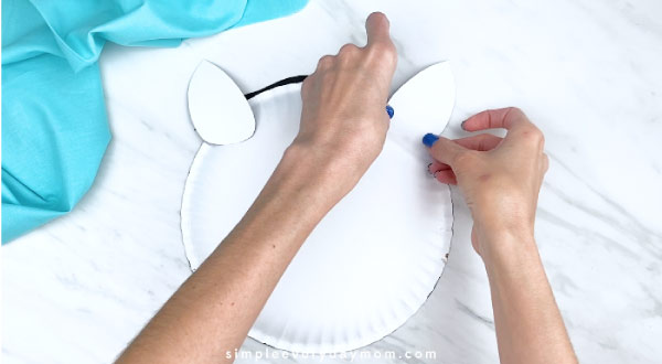 Hands taping ears to back of paper plate horse 