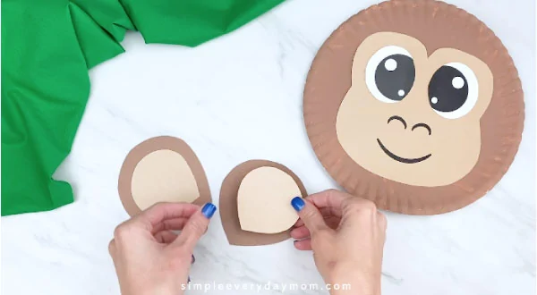 hands gluing on inner ear to outer ear with monkey paper plate to the right 