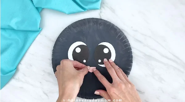 Hand gluing nose onto gray paper plate 