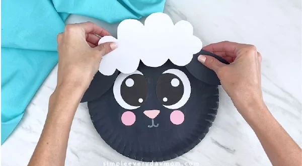 Hands gluing sheep fluff and ears to paper plate 