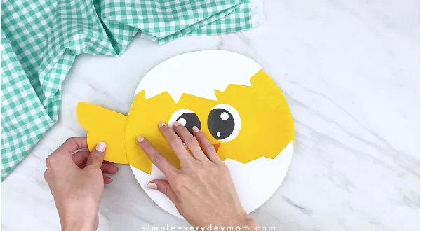 Hands gluing wings to paper plate chick 