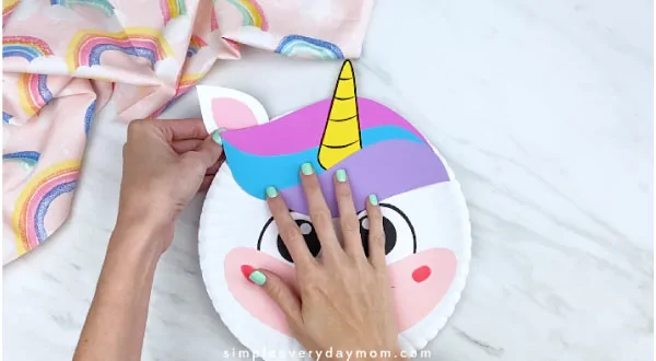 hands taping finished unicorn ear to back of paper plate unicorn 