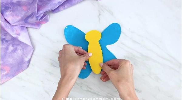 Hands gluing yellow body onto blue butterfly wings 