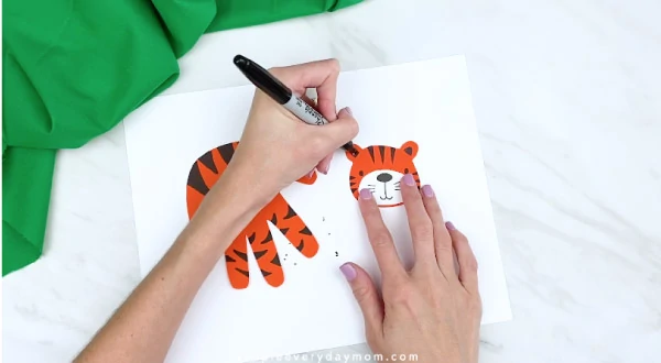 hands coloring in tiger ears with black marker 