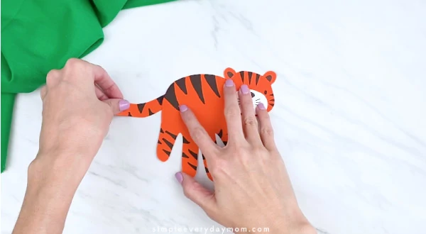 hands gluing on tail to handprint tiger craft 