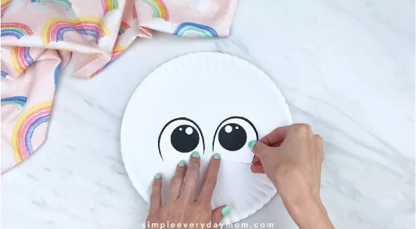 hands gluing on eyes to white paper plate 