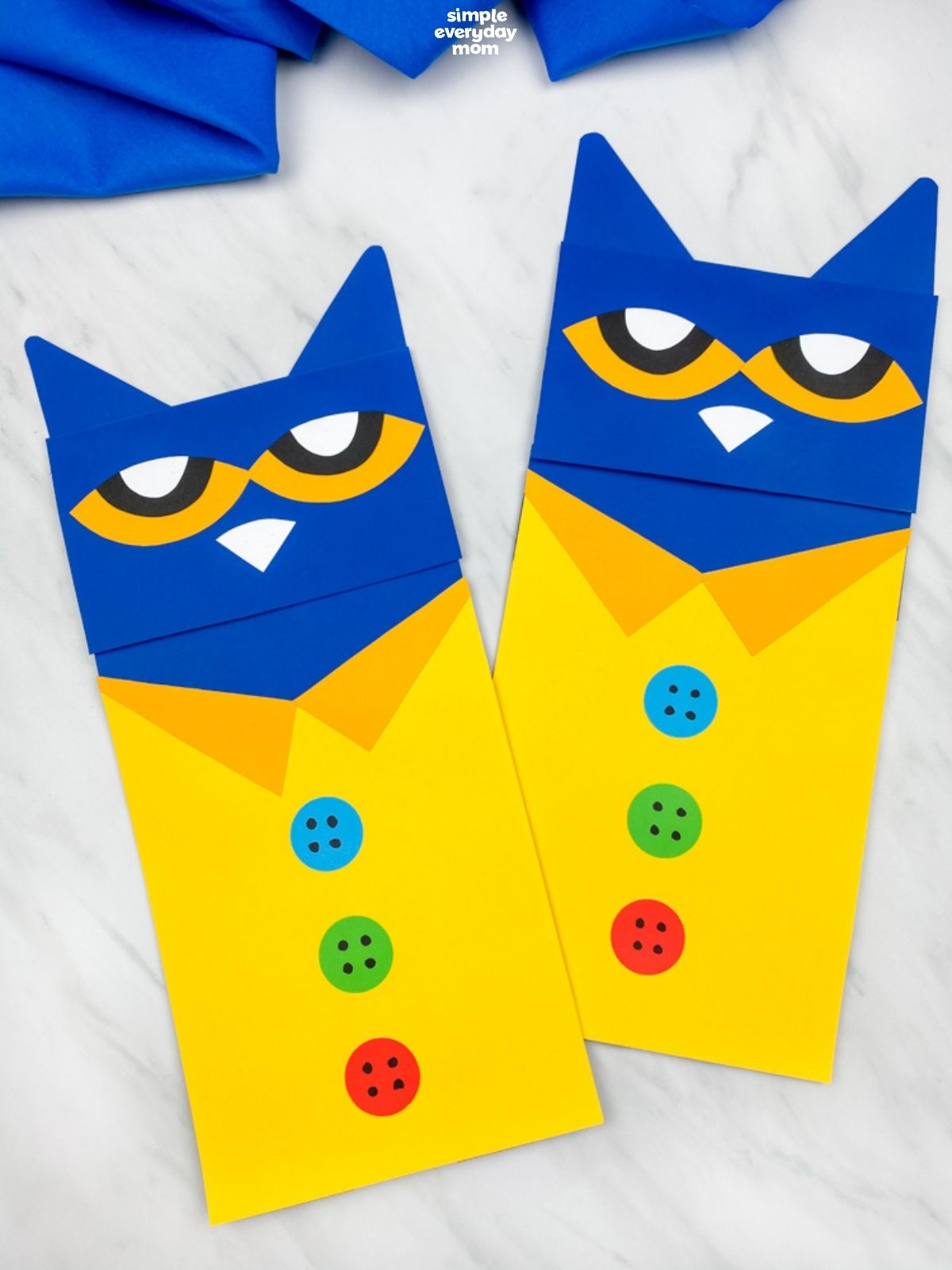 Two completed Pete the Cat paper crafts displayed side by side, featuring blue faces, yellow shirts, and blue, green, and red buttons.