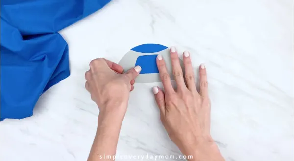 hands gluing on blue paper to R2D2 craft 