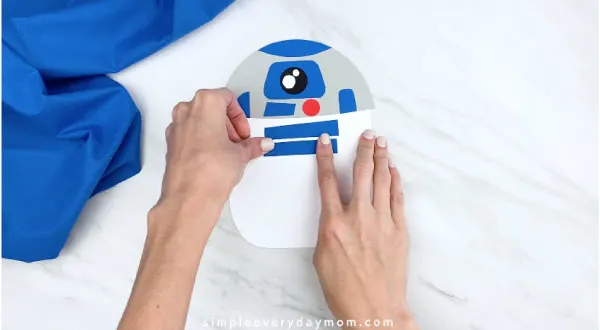 hands gluing on blue rectangles onto R2D2 