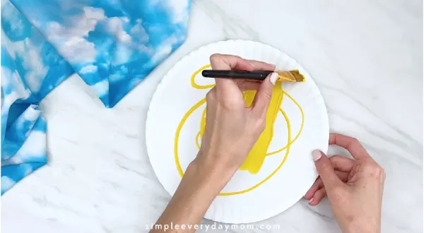hands painting white paper plate yellow 