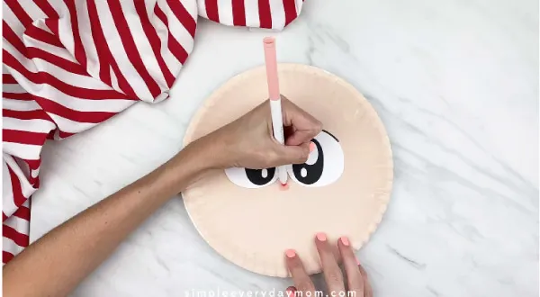 hands drawing nose on paper plate pirate with dark peach marker 