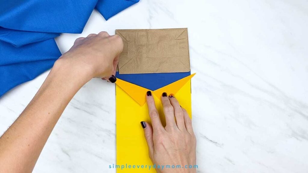 Hands position an orange paper collar over the yellow shirt on the Pete the Cat puppet.