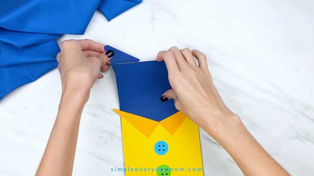 Hands attach a triangular dark blue paper ear to the top of the puppet’s head.
