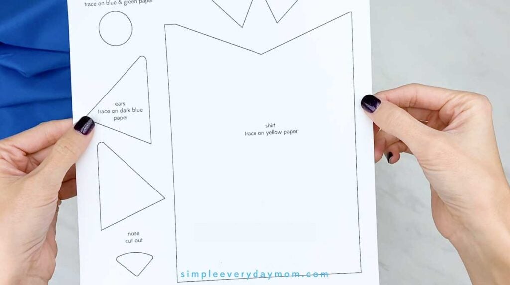 Hands hold a printable Pete the Cat craft template with outlined pieces for the shirt, ears, nose, and other features.
