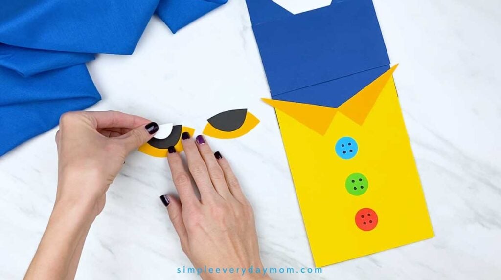 Hands add a white paper section to the black-and-yellow eye piece for the Pete the Cat puppet.
