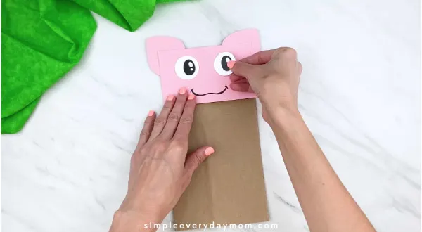 hands gluing on eye to paper bag pig craft