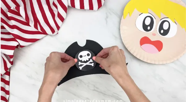 hands gluing on skull and crossbones to pirate hat 