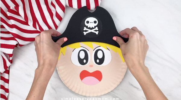 hands gluing on pirate hat to paper plate pirate 