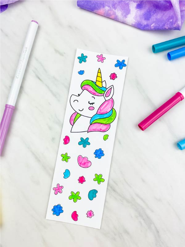 one coloring page unicorn bookmark on marble background with markers and purple fabric 