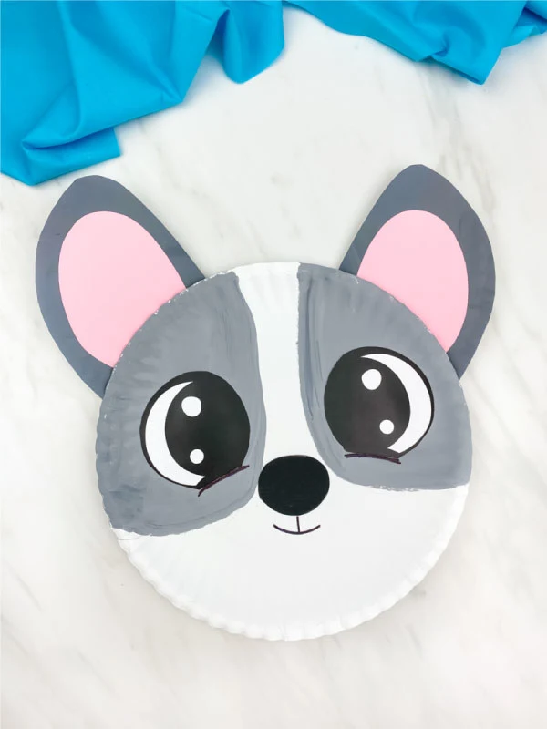 gray paper plate dog craft on marble background with blue fabric 