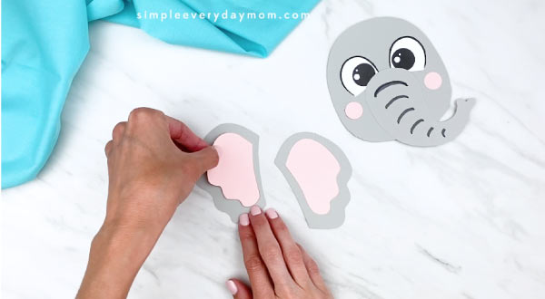 hands gluing inner ear onto outer ear of elephant paper craft