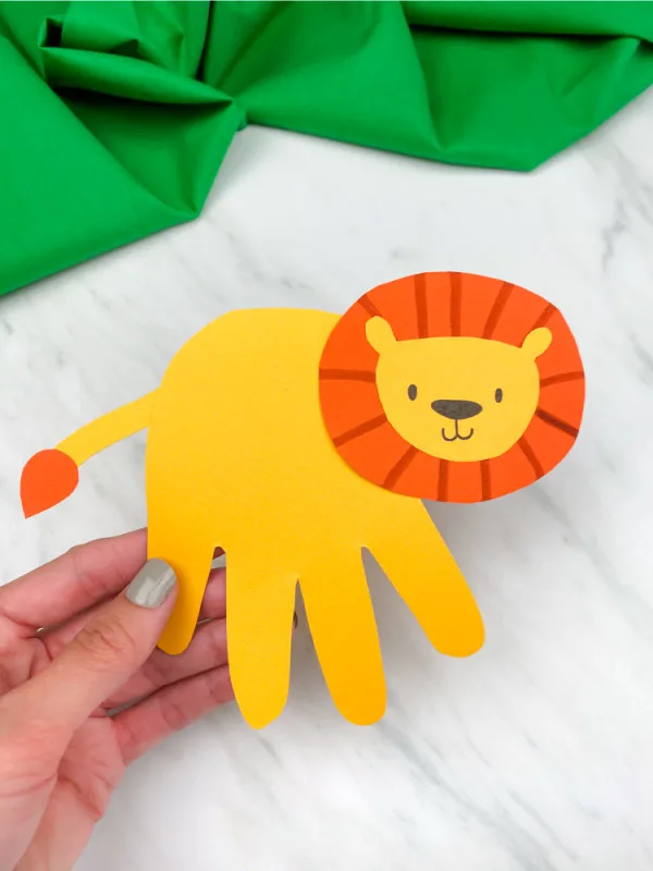 hand holding handprint lion craft with marble background and green fabric
