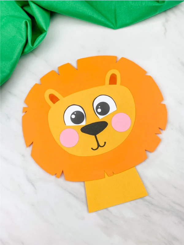 paper lion craft with light orange mane on marble background with green fabric 