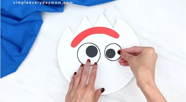 hands gluing on forky's eyes to paper plate 