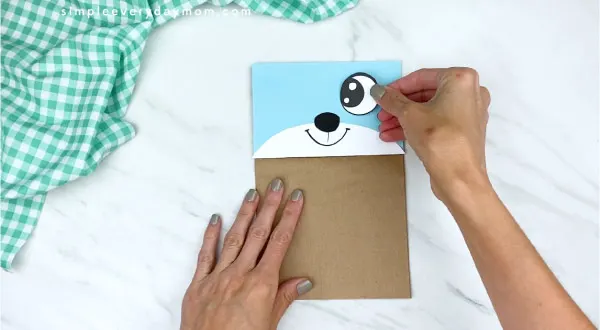 hands gluing on eyes to paper bag mouse craft 