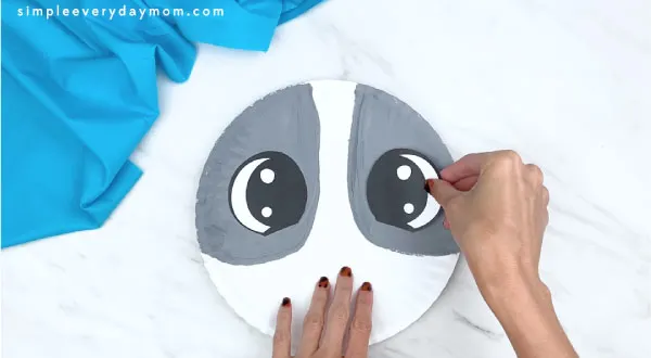 hands gluing eyes onto gray parts of paper plate 