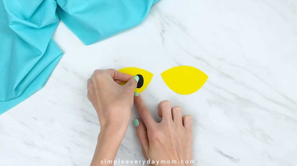 Hands attaching a black pupil to a yellow paper eye.