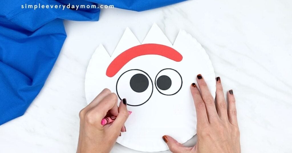 Hand coloring pink cheeks onto a paper plate Forky craft.