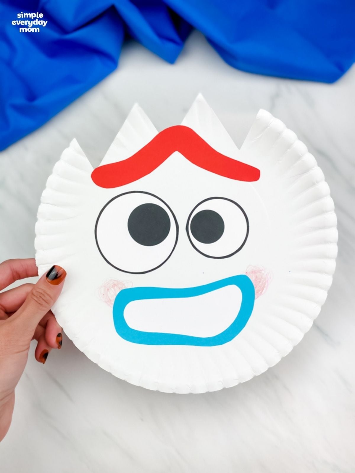 Hand holding a finished smiling Forky paper plate craft.